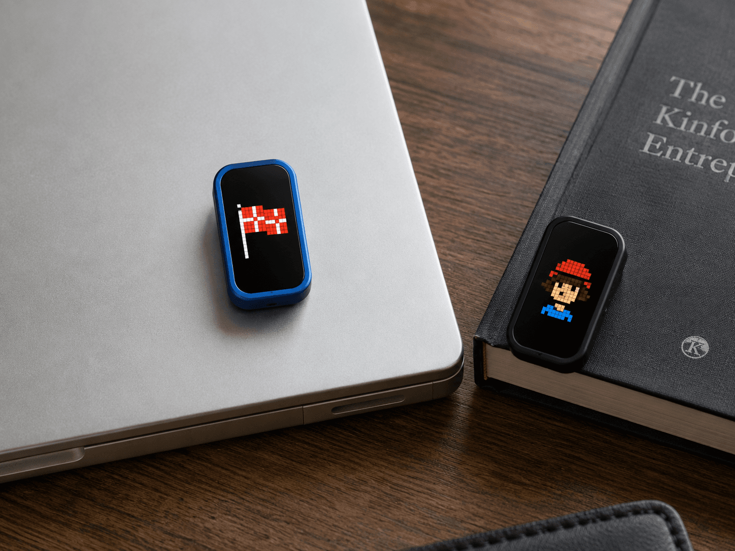 Two MoodPin units on a desk, one magnetised to a laptop lid and one propped against a hardback book