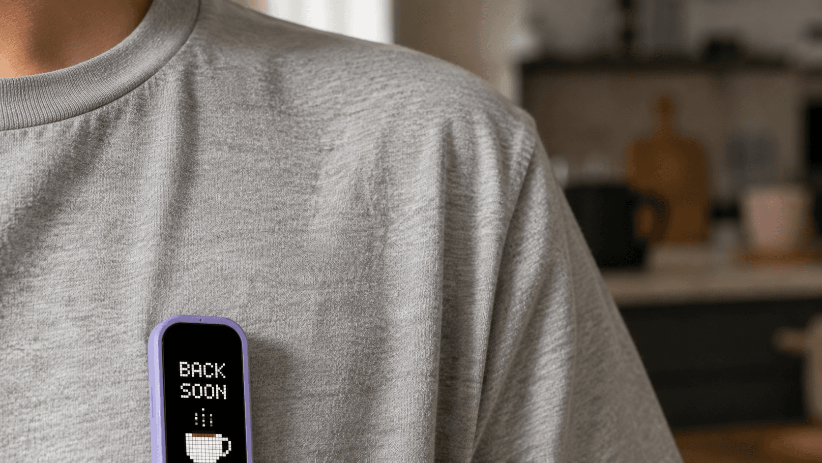 A lavender MoodPin on a grey t-shirt showing BACK SOON above a pixel coffee cup